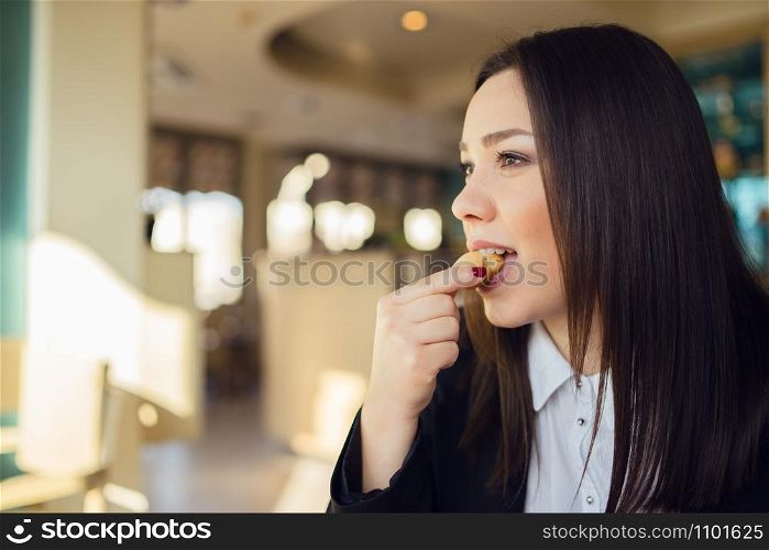 Portrait of young woman sitting by the table at cafe or office eating cookie during the brake