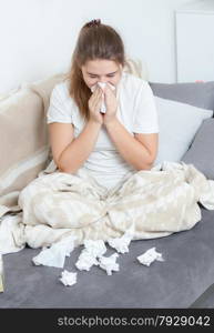 Portrait of young woman sitting on couch and blowing nose