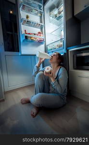 Portrait of young woman sitting on floor at kitchen and having late dinner