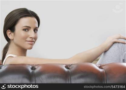Portrait of young woman sitting on sofa against gray background