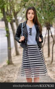 Portrait of young woman smiling in urban background wearing casual clothes. Girl wearing striped skirt, sweater and leather jacket