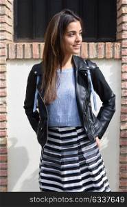 Portrait of young woman smiling in urban background wearing casual clothes. Girl wearing striped skirt, sweater and leather jacket