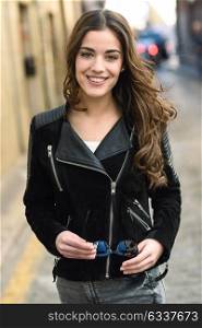 Portrait of young woman smiling in urban background wearing casual clothes with long curly hair