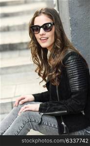 Portrait of young woman smiling in urban background wearing casual clothes with modern sunglasses. Girl with long curly hair