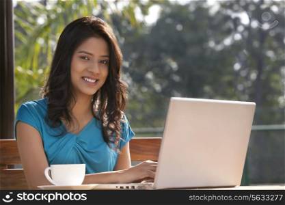 Portrait of young woman smiling while using laptop