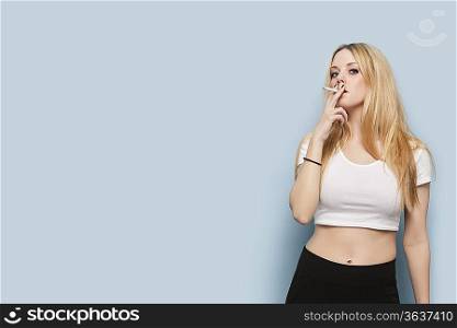 Portrait of young woman smoking cigarette against light blue background