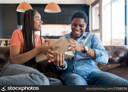 Portrait of young woman surprising her boyfriend with a gift box. Celebration and valentine&rsquo;s day concept.