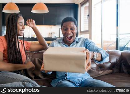 Portrait of young woman surprising her boyfriend with a gift box. Celebration and valentine&rsquo;s day concept.