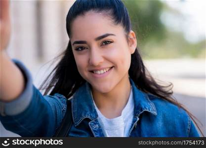 Portrait of young woman taking selfies while standing outdoors on the street. Urban concept.