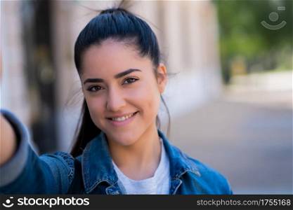 Portrait of young woman taking selfies while standing outdoors on the street. Urban concept.