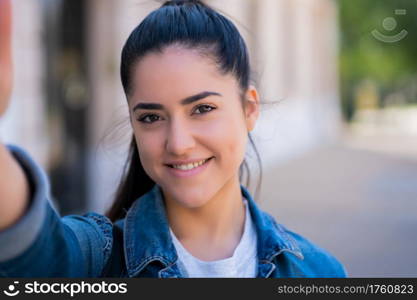 Portrait of young woman taking selfies while standing outdoors on the street. Urban concept.