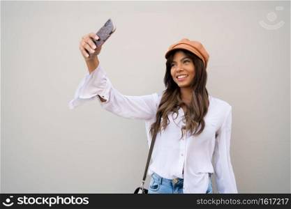 Portrait of young woman taking selfies with her mophile phone while standing outdoors. Urban concept.