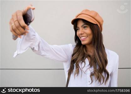 Portrait of young woman taking selfies with her mophile phone while standing outdoors. Urban concept.