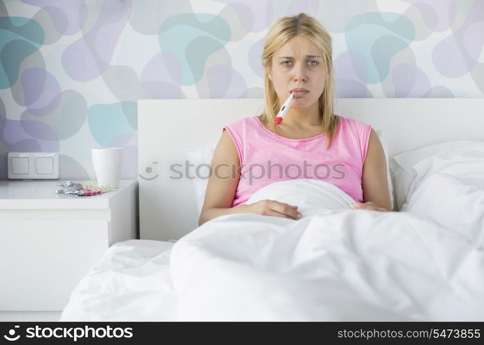 Portrait of young woman taking temperature with thermometer