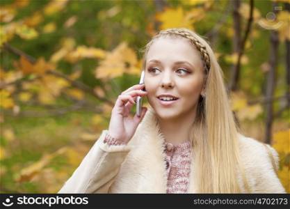 Portrait of young woman talking on mobile phone in autumn park