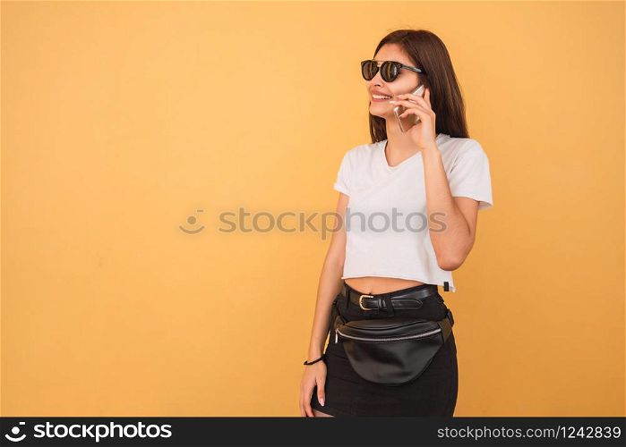 Portrait of young woman talking on the phone against yellow background. Urban and communication concept.
