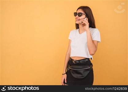 Portrait of young woman talking on the phone against yellow background. Urban and communication concept.