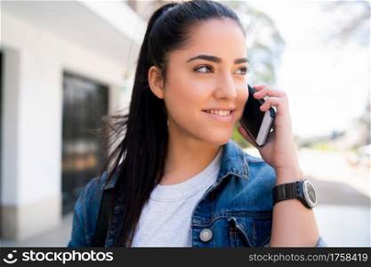 Portrait of young woman talking on the phone while standing outdoors on the street. Urban and communication concept.