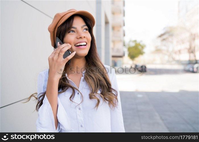 Portrait of young woman talking on the phone while standing outdoors on the street. Urban and communication concept.