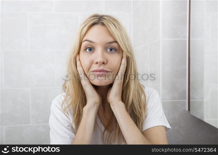 Portrait of young woman touching cheeks in bathroom