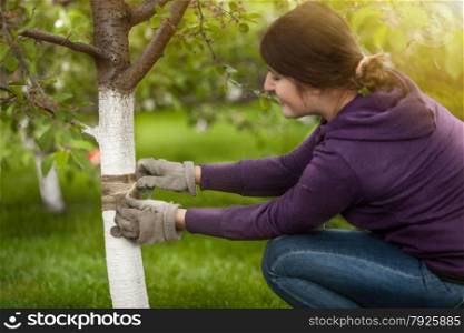 Portrait of young woman tying band on tree bark to prevent insects