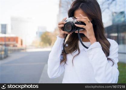 Portrait of young woman using a professional digital camera while standing outdoors on the street. Photography concept