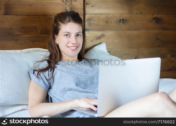Portrait of young woman using her laptop while lying on the bed at home. Lifestyle concept