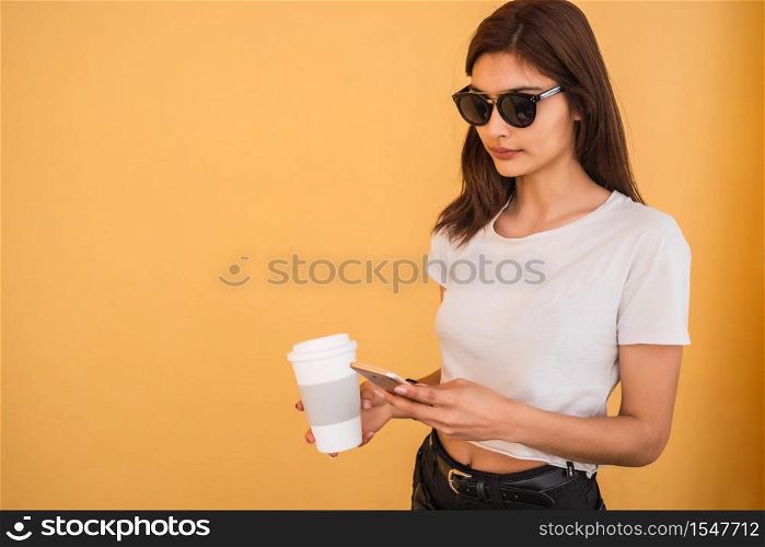 Portrait of young woman using her mobile phone while holding a cup of coffee outdoors in the street. Urban and communication concept.