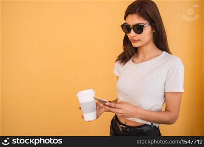 Portrait of young woman using her mobile phone while holding a cup of coffee outdoors in the street. Urban and communication concept.