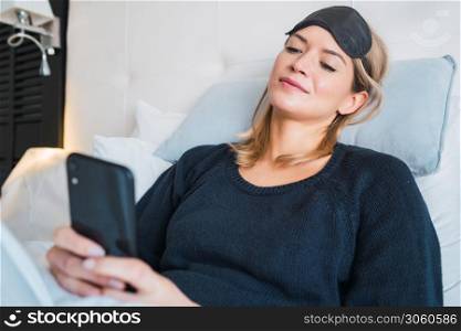 Portrait of young woman using her mobile phone while laying on bed at hotel room. Travel and lifestyle concept.