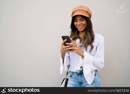 Portrait of young woman using her mobile phone while standing outdoors on the street. Urban and communication concept.