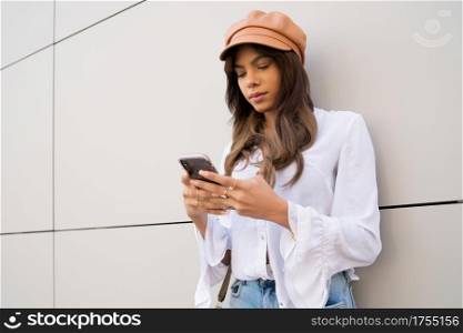 Portrait of young woman using her mobile phone while standing outdoors on the street. Urban and communication concept.
