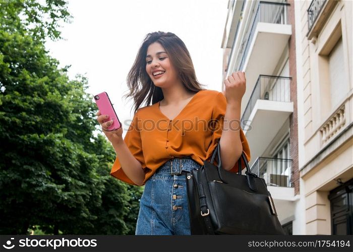 Portrait of young woman using her mobile phone while walking outdoors on the street. Urban and communication concept.
