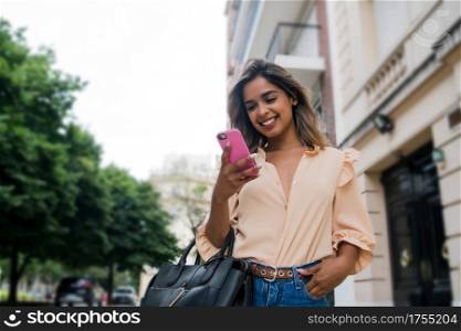 Portrait of young woman using her mobile phone while walking outdoors on the street. Urban and communication concept.