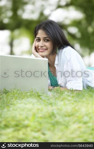 Portrait of young woman using laptop while lying on grass