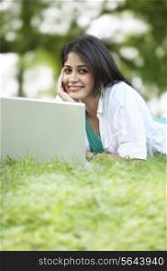Portrait of young woman using laptop while lying on grass