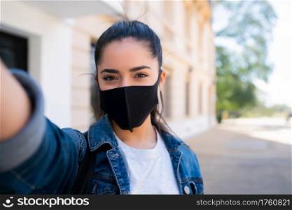 Portrait of young woman wearing face mask and taking selfies outdoors. Urban concept. New normal lifestyle concept.