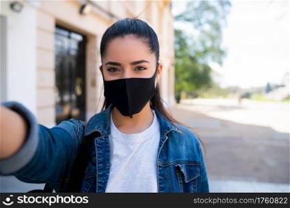Portrait of young woman wearing face mask and taking selfies outdoors. Urban concept. New normal lifestyle concept.