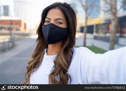 Portrait of young woman wearing face mask and taking selfies while standing outdoors on the street. Urban concept. New normal lifestyle concept.