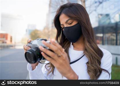 Portrait of young woman wearing protective mask and using camera while taking photographs in the city. New normal lifestyle concept.