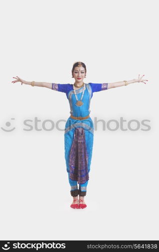 Portrait of young woman with arms outstretched performing Bharatanatyam against white background