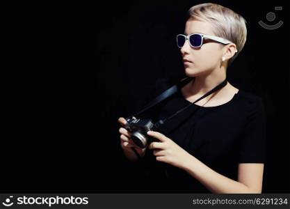 Portrait of young woman with camera on black background