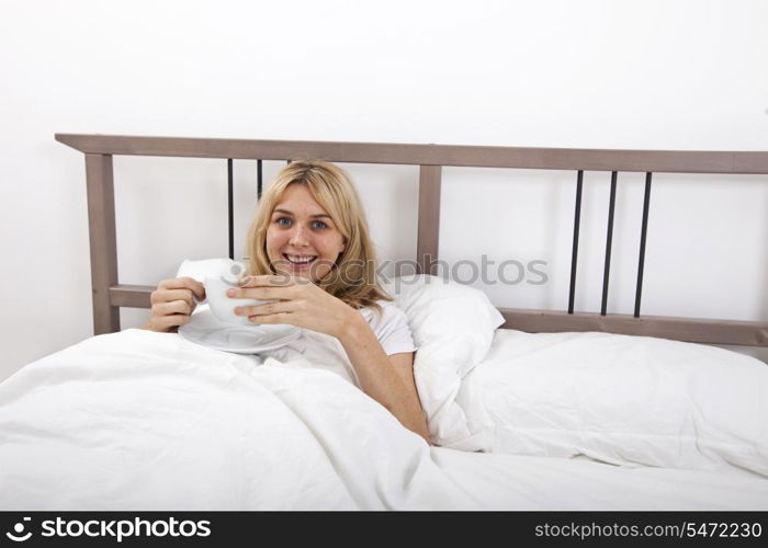 Portrait of young woman with coffee cup in bed