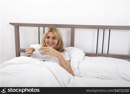 Portrait of young woman with coffee cup in bed