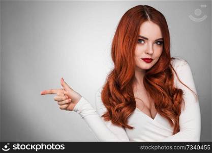 Portrait of young woman with long beautiful ginger hair pointing aside. Woman with long ginger hair