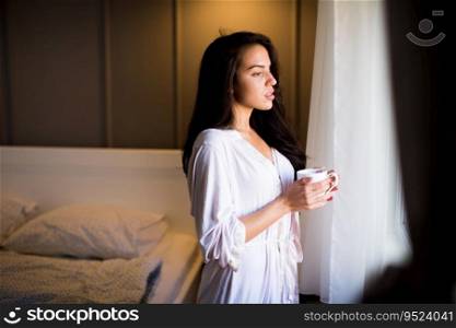 Portrait of young woman with mug in bedroom