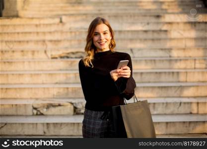 Portrait of young woman with shopping bag and mobile phone outdoor