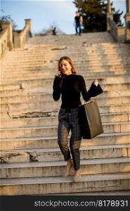 Portrait of young woman with shopping bag using mobile phone outdoor