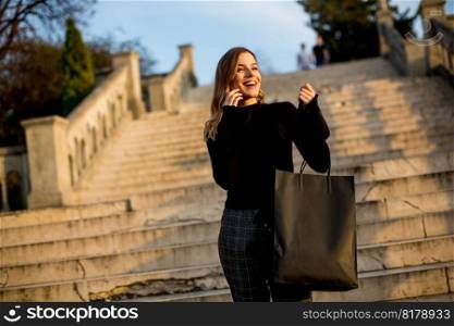 Portrait of young woman with shopping bag using mobile phone outdoor