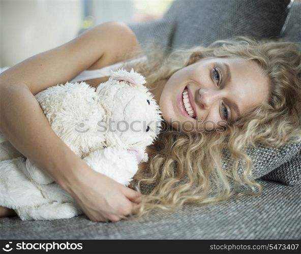 Portrait of young woman with teddy bear lying on sofa